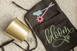 An apron with Bloom written on it, plant sticks, and a pot