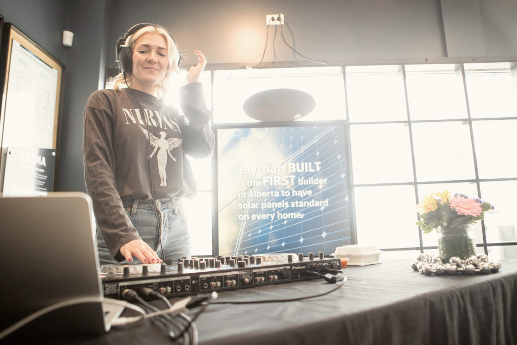 A DJ stands in front of a laptop and sound board