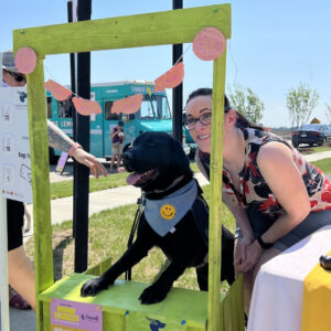 A dog peeks through a lemonade stand with it's handler by its side